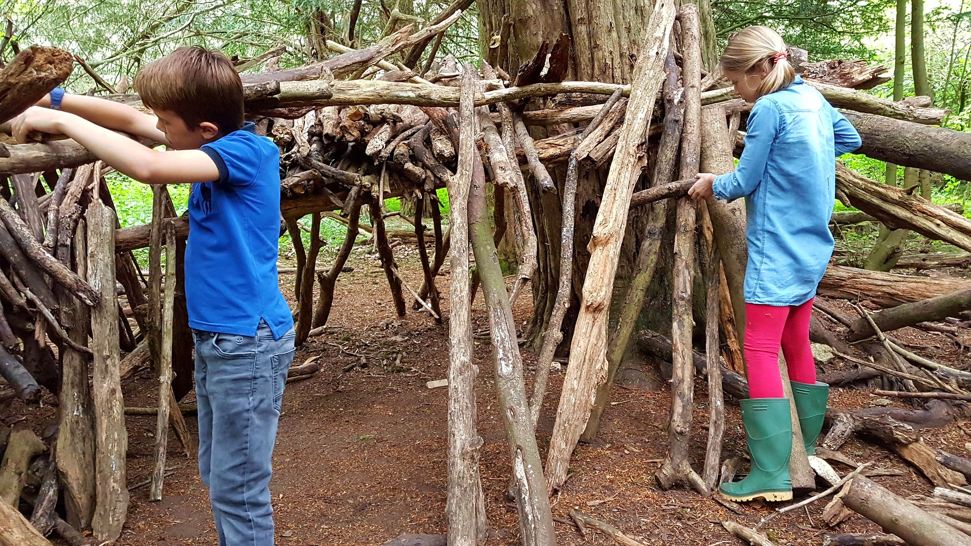 Niño y niña haciendo una cabaña con troncos